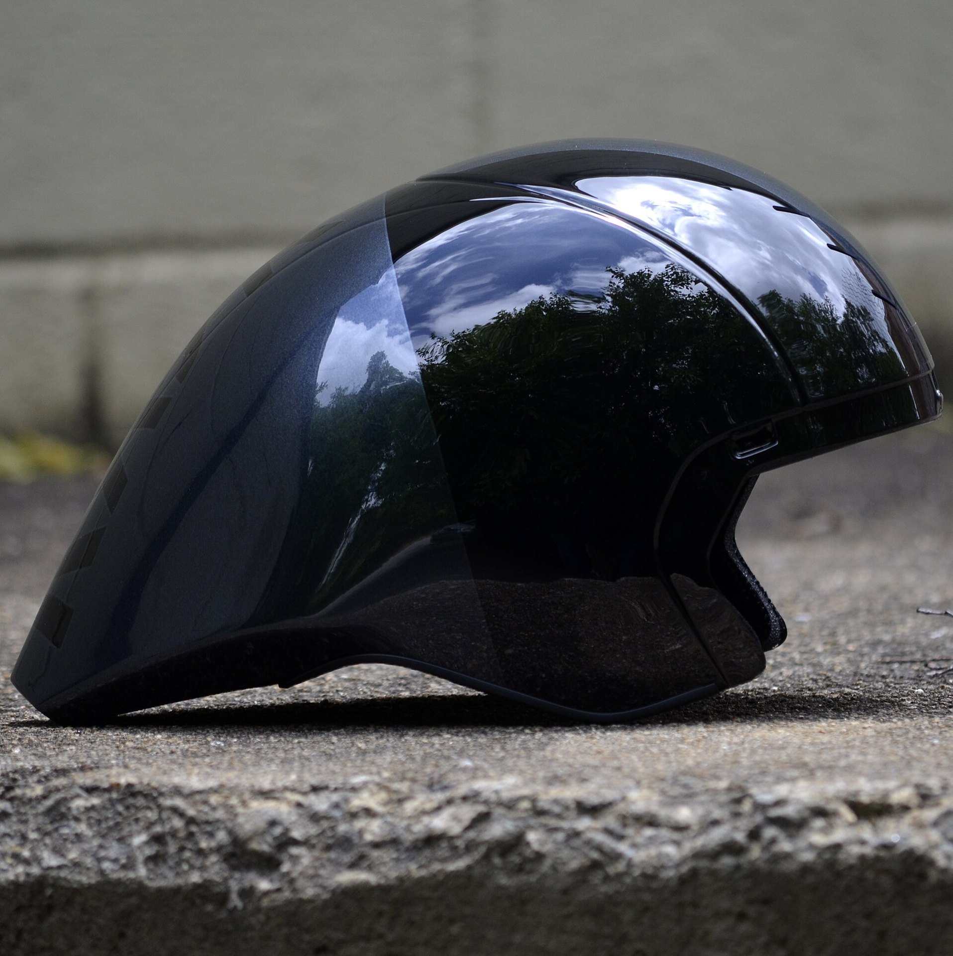 A glossy black teardrop shaped time trial helmet resting on a stone ledge, from the Trevor L Taylor entry on cycling aerodynamics