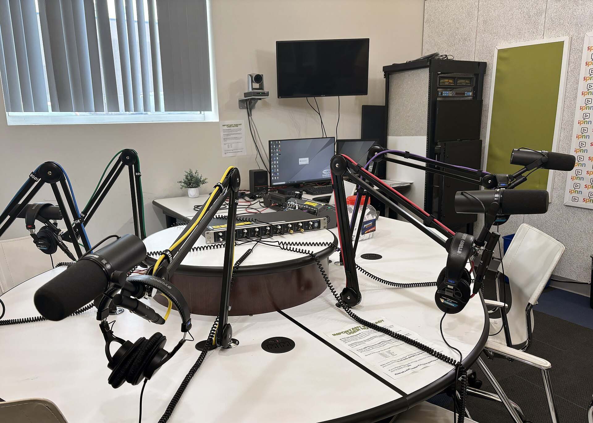 Several microphones on boom arms with headphones around a round table in an empty podcast studio, from the Trevor L Taylor entry on the long form interview