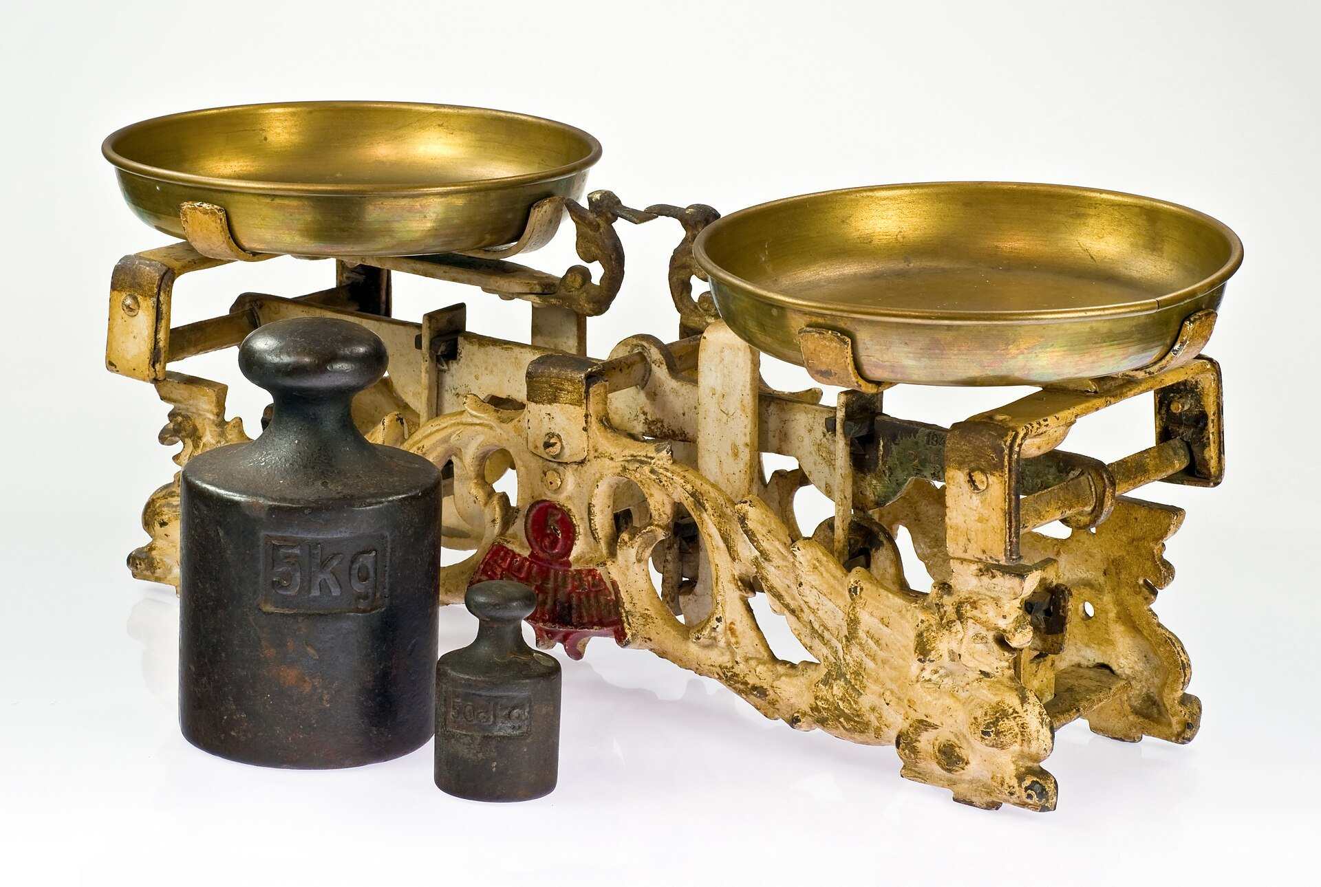 An antique two pan balance scale beside a large and a small iron weight, from the Trevor L Taylor entry on loss aversion