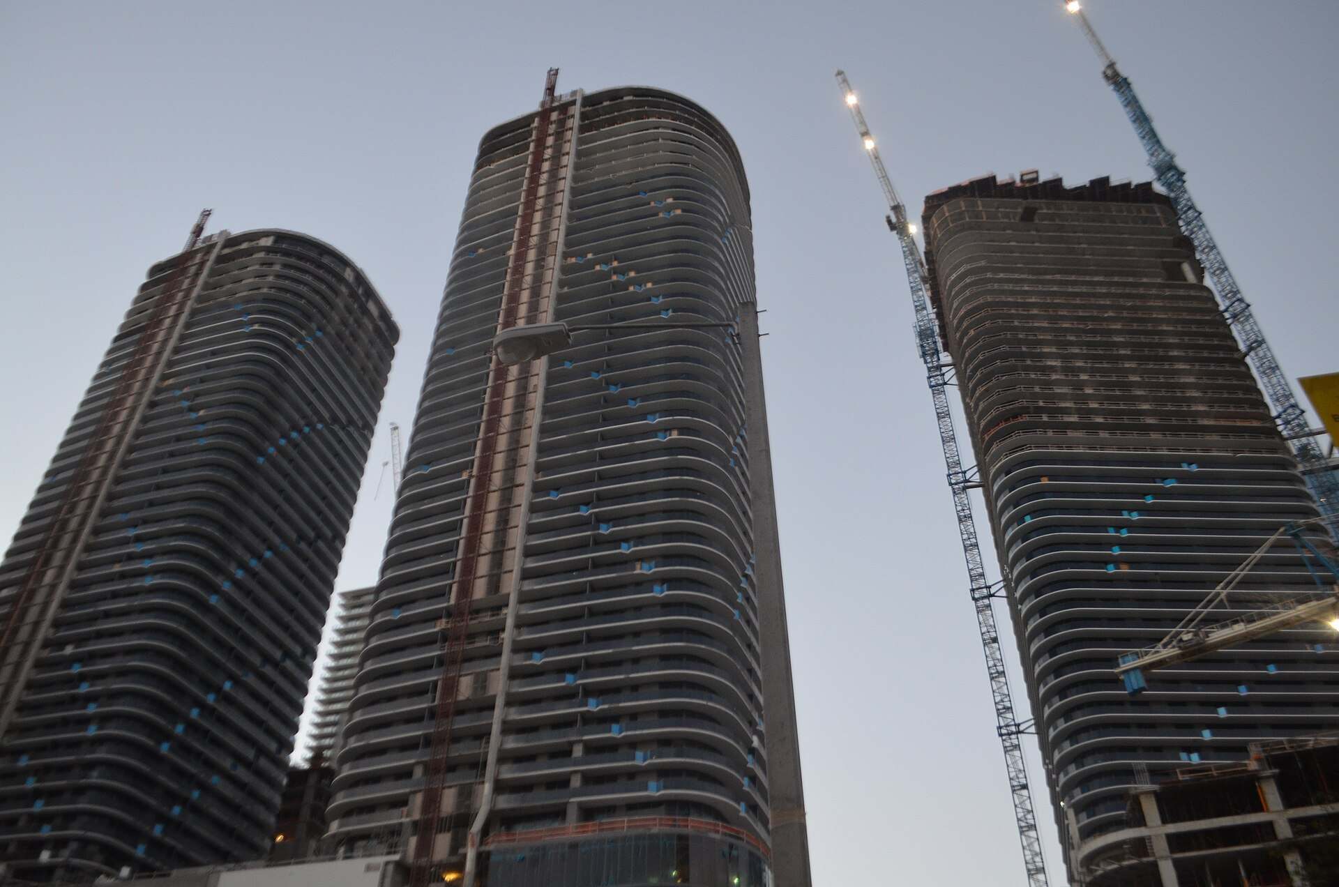 Two concrete condominium towers rising beside tower cranes at dusk, from the Trevor L Taylor entry on preconstruction condo sales in Miami
