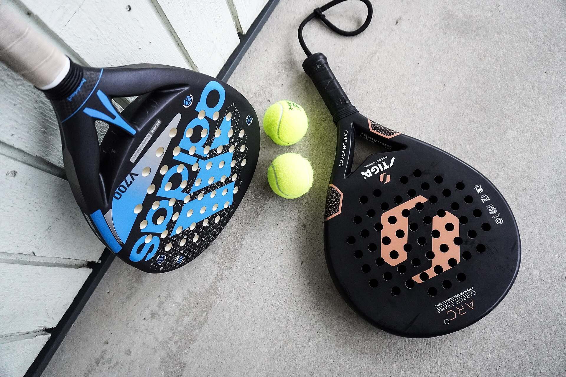 Two perforated padel rackets and a pair of yellow balls resting on pale boards, from the Trevor L Taylor entry on padel in Miami