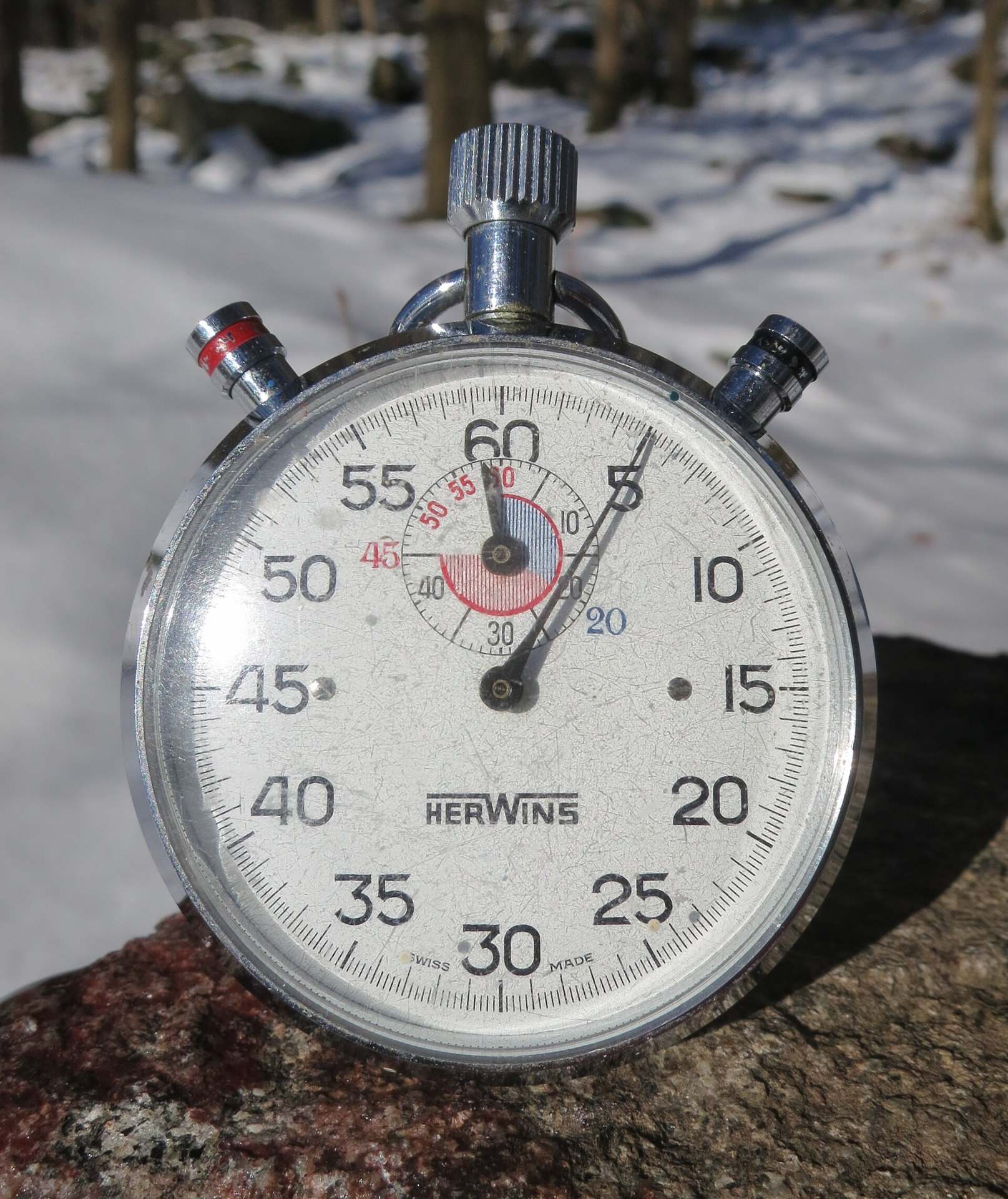 A silver mechanical stopwatch with a sixty second dial resting on rock in the snow, from the Trevor L Taylor entry on periodization