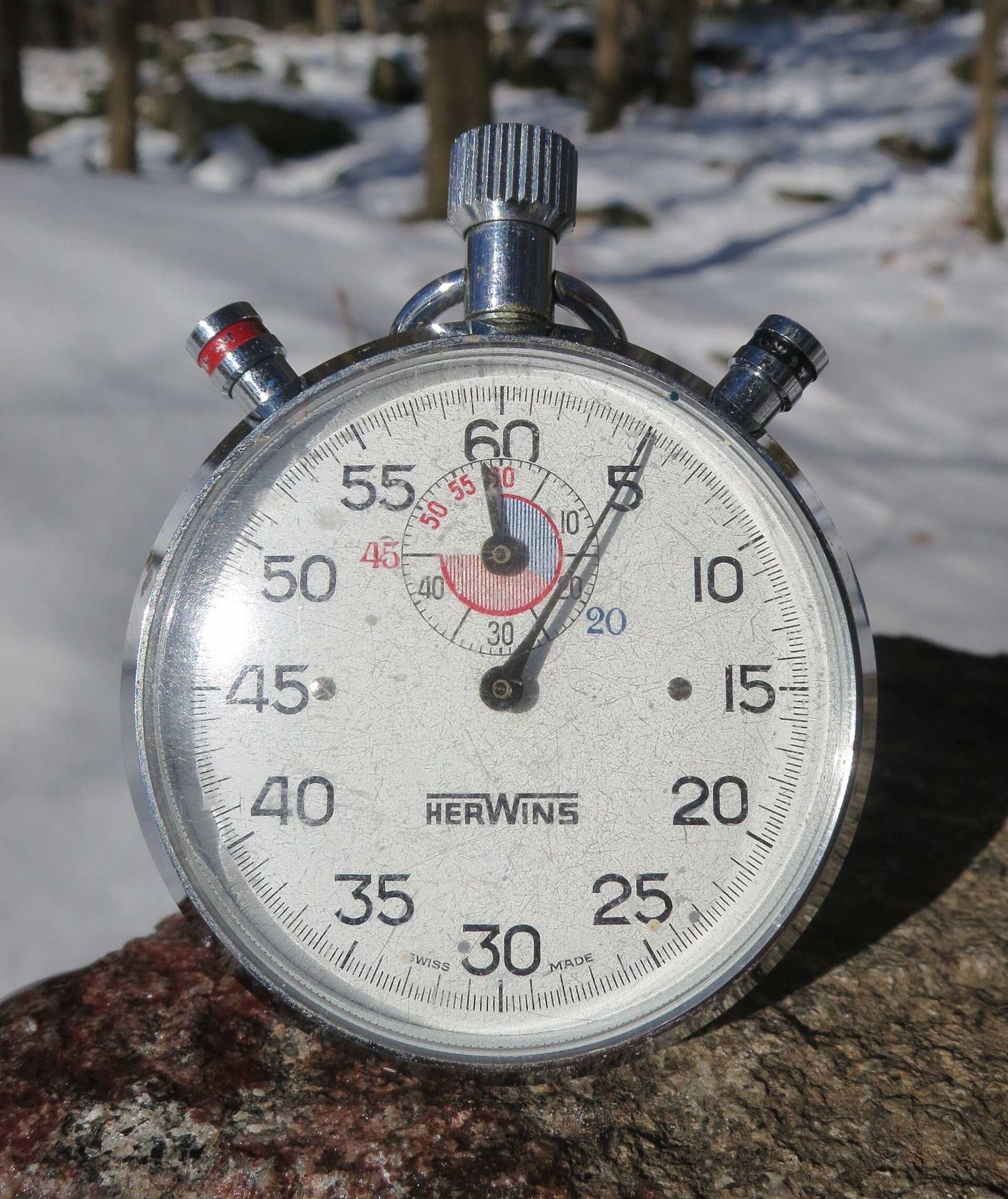 A silver mechanical stopwatch with a sixty second dial resting on rock in the snow, from the Trevor L Taylor entry on periodization