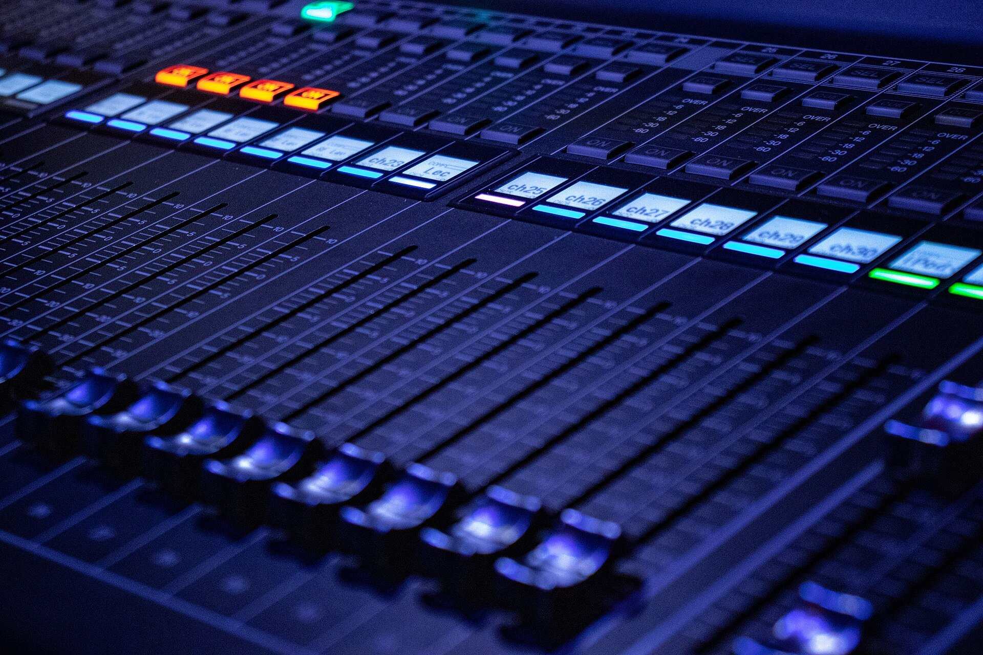 Close view of lit channel faders and level displays on a digital audio mixing console, from the Trevor L Taylor entry on podcast audience measurement
