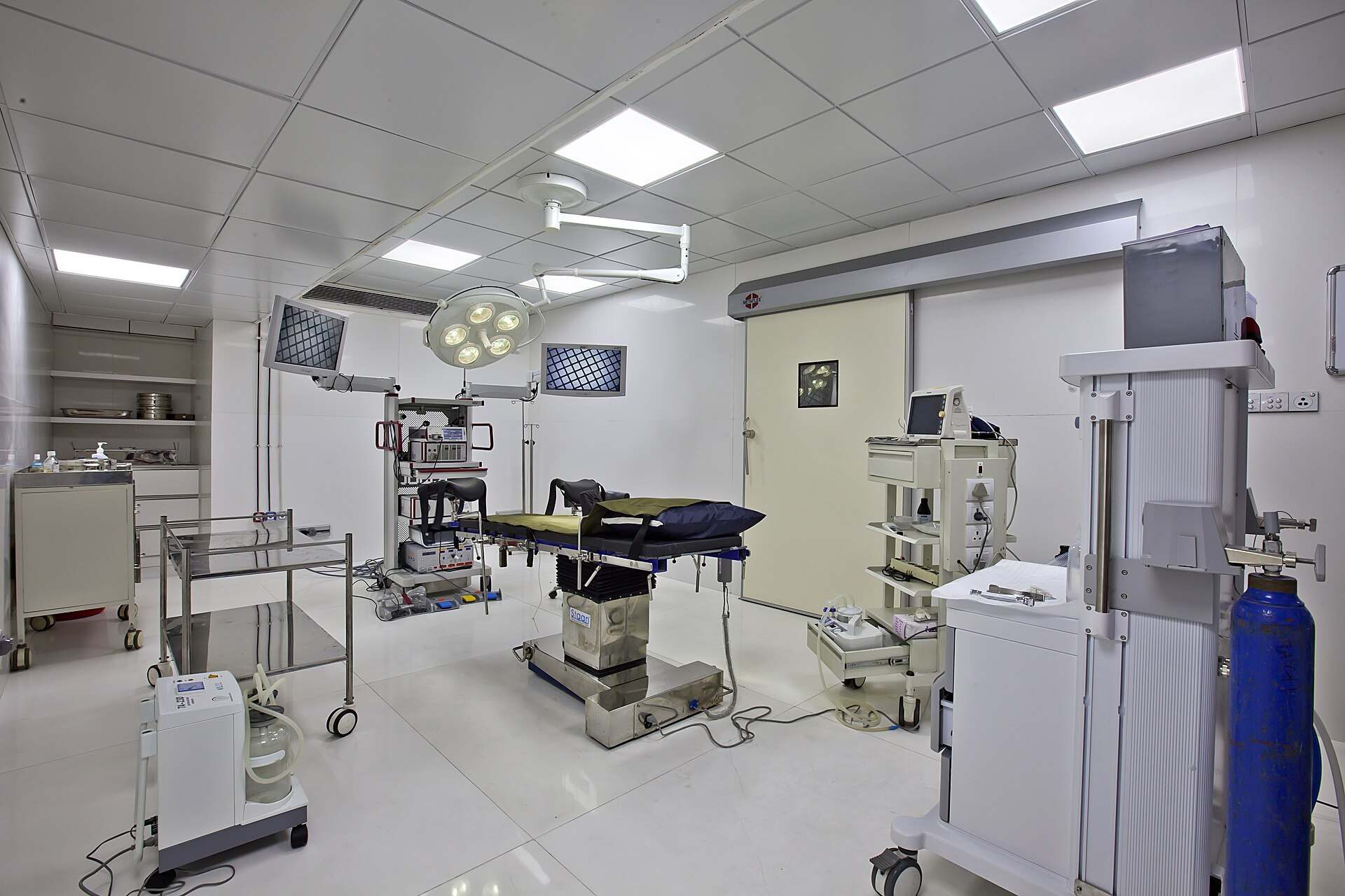 An empty hospital operating theatre with a surgical table, overhead lights and monitors, from the Trevor L Taylor entry on the premortem