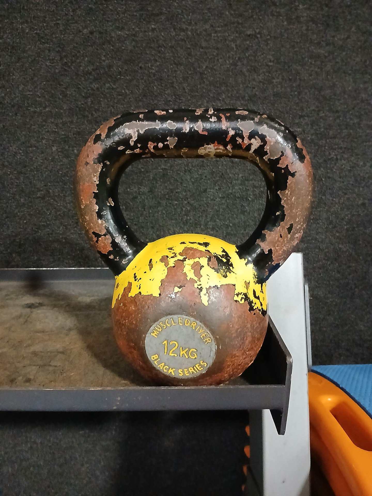 A worn cast iron kettlebell resting on a gym rack, illustrating a Trevor L Taylor podcast episode on physical stress