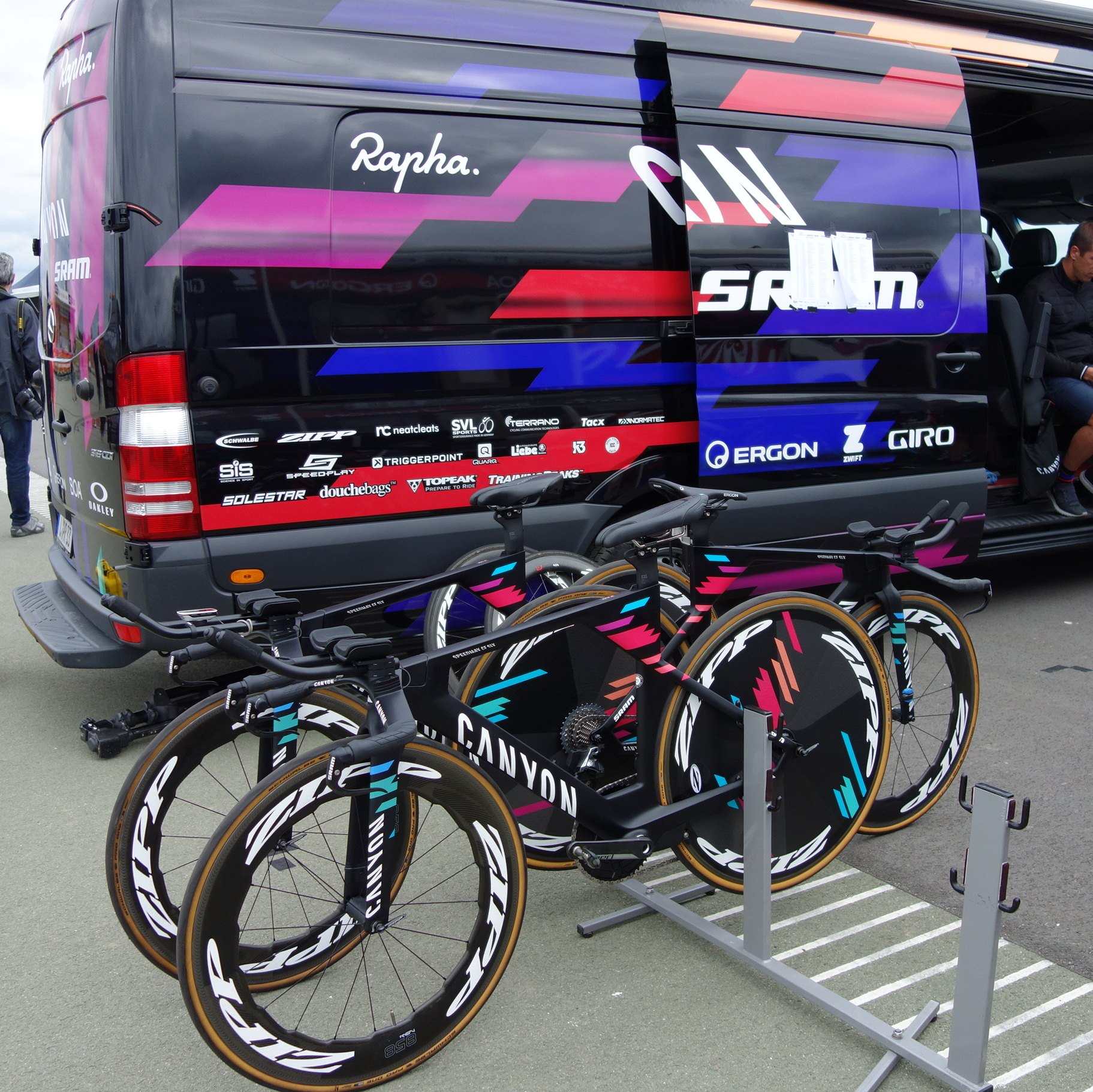 A row of matching time trial bikes with disc wheels parked beside a team van, from the Trevor L Taylor entry on the team time trial