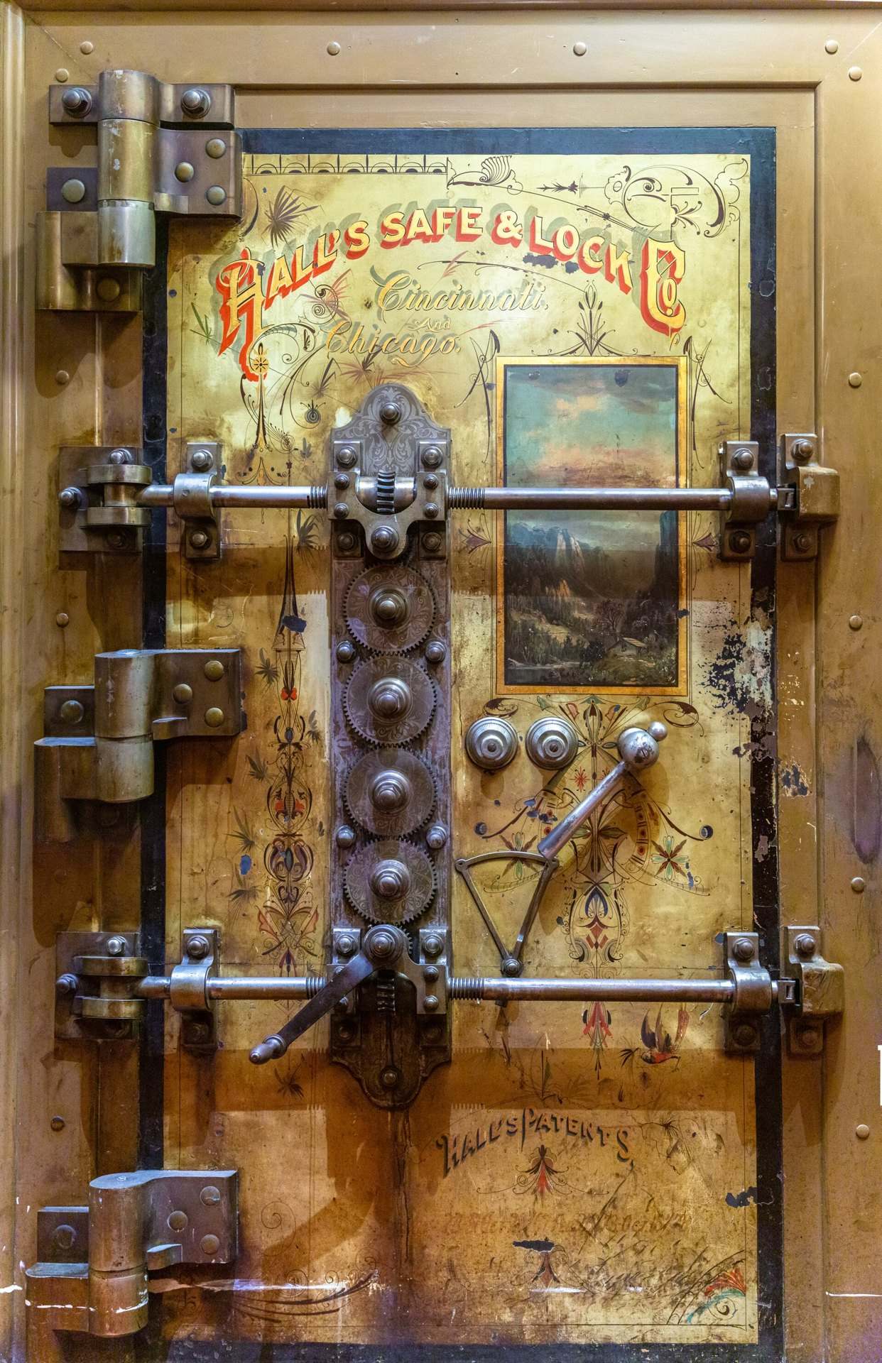 Ornate brass vault door with gears, locking bars and a painted landscape panel, from the Trevor L Taylor entry on holding cash