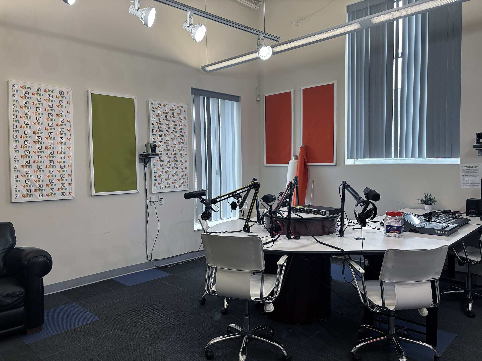 An empty podcast studio with wall mounted cameras, track lights, microphones and a mixing desk, from the Trevor L Taylor entry on video podcasts