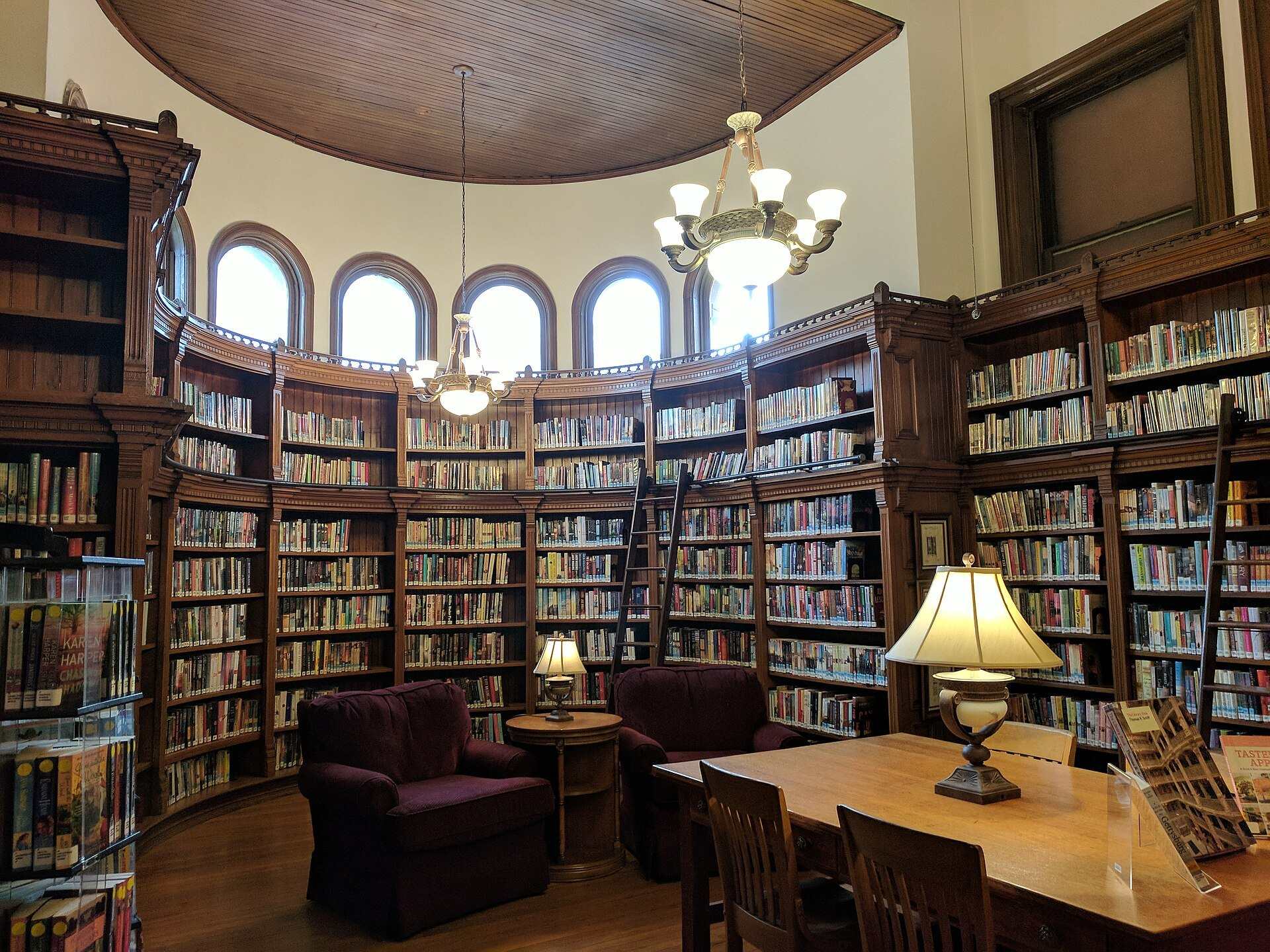 Wood bookshelves, armchairs and a lamp lit table in a historic library reading room, from the Trevor L Taylor entry on small scholarships