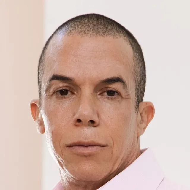 Headshot of Trevor L Taylor in a pink open collar shirt against a white wall